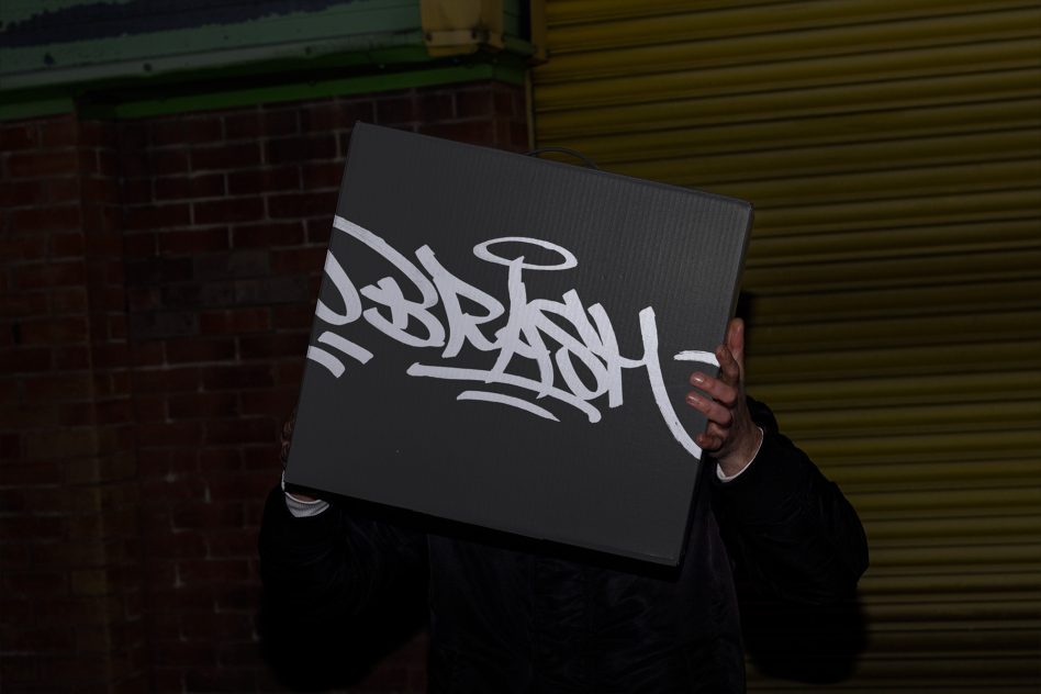 Person holding canvas with graffiti-style lettering, potential mockup or graphic element, urban design, nighttime backdrop for designers.